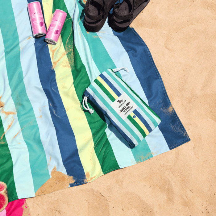 Dock & Bay Color Canyon striped towel on the sand with matching pouch and drinks nearby, highlighting beach-ready design