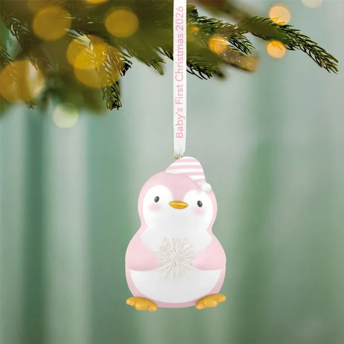 Close-up of hanging pink penguin ornament with Baby's First Christmas 2026 ribbon text