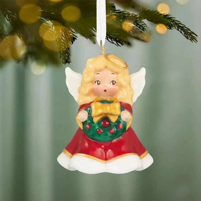 Red and white angel Christmas tree ornament hanging on pine branch
