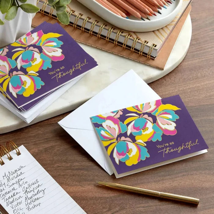 Colorful floral card with 'You're so thoughtful' message on a wooden surface with stationery items.