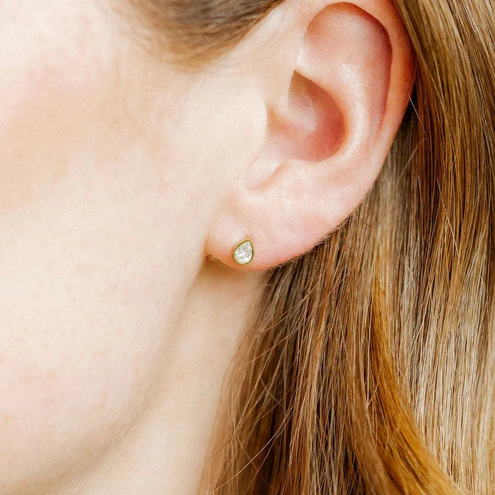 The Paloma Pear Gold Screwback Stud Earrings. Featuring a stunning pear-shaped CZ stone set in a sleek gold bezel, these earrings offer a timeless, refined design that adds a touch of elegance to any outfit.