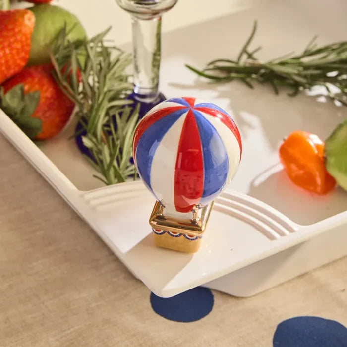 Decorative hot air balloon on a white surface with strawberries and rosemary in the background.