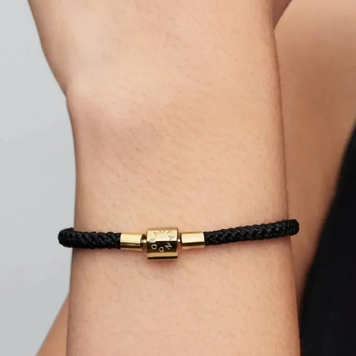 Close-up of a woman’s wrist wearing the Pandora Shimmering Black Cord Bracelet featuring a black cord and gold-plated clasp.