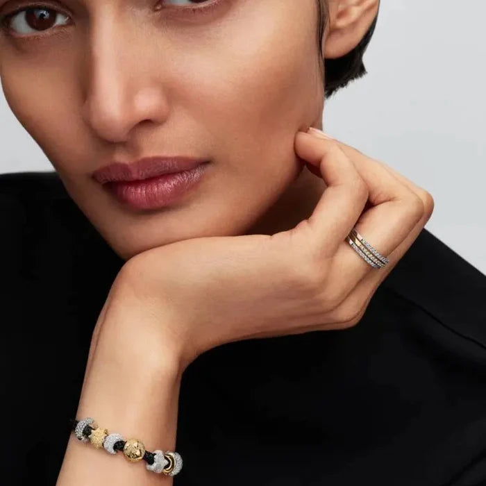 Close-up of a woman’s wrist wearing the Pandora Shimmering Black Cord Bracelet in black cord with gold-plated clasp, adorned with charms.