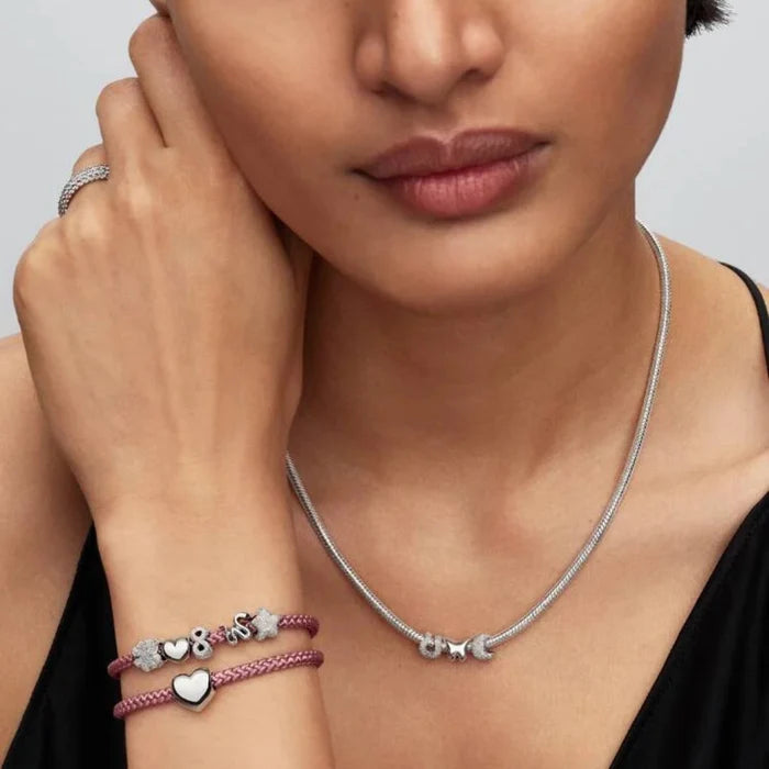 Close‑up of a woman’s wrist wearing a pink cord bracelet with a silver charm
