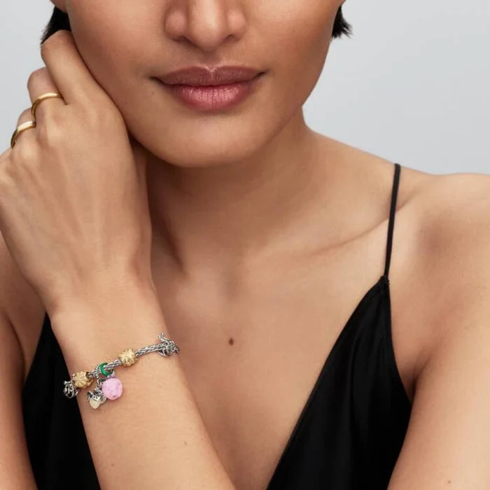 A woman displays a pink bracelet and a gold bracelet on her wrist, showcasing her stylish accessories.