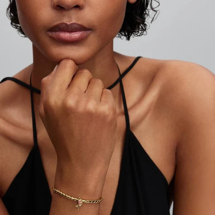 A woman showcases a gold bracelet adorned with a pink diamond, highlighting her elegant style and fashion choice.